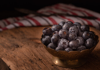 Blueberries in vintage metal bowl on rustic wooden background. Dark mood photo. Selective focus, copy space