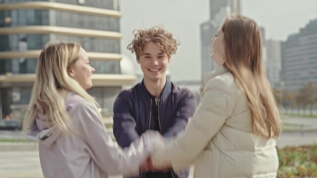Side view of a happy group of Caucasian boy and girls outdoors together on a sunny day, in a huddle, hand stacking