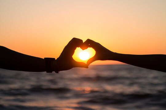 Pareja en la playa haciendo un coraz&oacute;n en el atardecer.