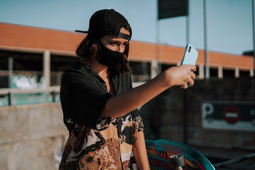 Chica joven urbana con mascarilla coronavirus pandemiua covid-19 en skatepark con patin skate...