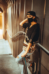 Chica joven urbana con mascarilla coronavirus pandemiua covid-19 en skatepark con patin skate...