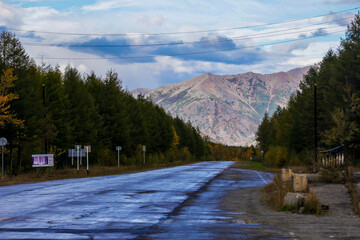 Fototapeta na wymiar The nature of the Magadan region. An asphalt road among bright trees, stretching into the distance to high hills