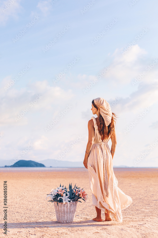 Wall mural beautiful young stylish woman with basket with flowers outdoors at sunset