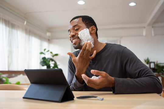 Black male shaving his beard and using digital tablet pretend to be mirror