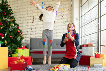 Asian mother and young daughter cerebrate christmas and new year with confetti or paper firework in living room at home. family together and relationship concept