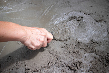 Mixed cement with sand , gravel and water by shovel, construction worker’s gloved hands using trowel to scrape the wall