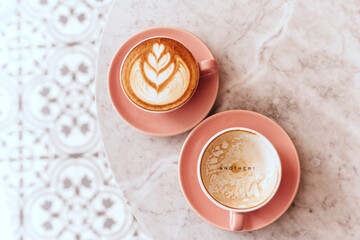Pink cup of cappuccino on marble table background. Love latte art on the top of it.