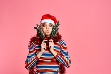 woman with christmas tree branches in hands red tinsel and festive hat pink background cropped view