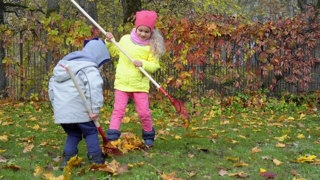 Brother and sister raking leafs in garden on an Autumn day