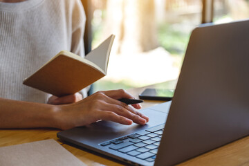 Fototapeta premium Closeup image of a woman writing on a notebook while working on laptop computer in office