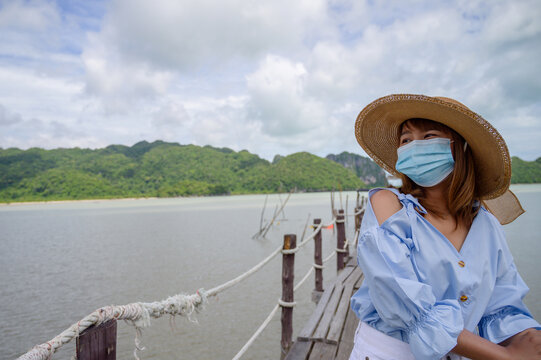 Young woman with protect face mask travel at the beach in Thailand with blue sky background and green islands