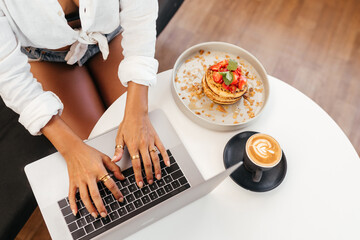 women hands at table with laptop near delicious pancakes with berries for breakfast