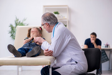 Young father and his daughter visiting old male doctor