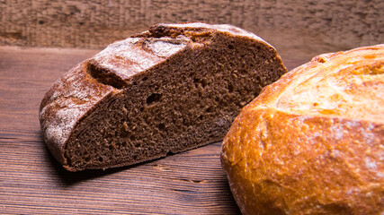 Half a loaf of rye bread and a whole loaf of white bread on an old wooden table,close-up
