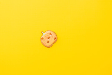 Sweet homemade pumpkin cookie with icing isolated on yellow background minimal flat lay composition.