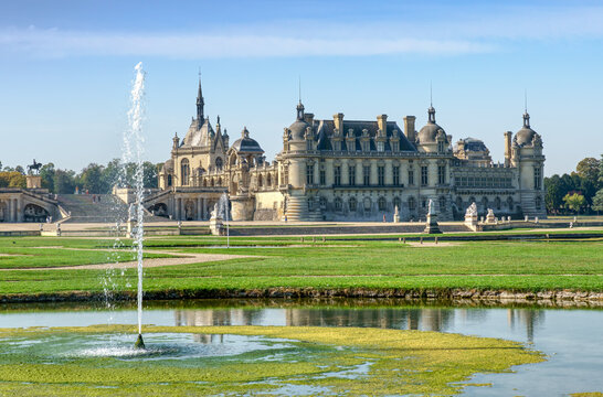 Chantilly, France - September 21 2020: View of the Chateau de Chantilly from Le Notre Garden with a fountain spraying water in the foreground - France