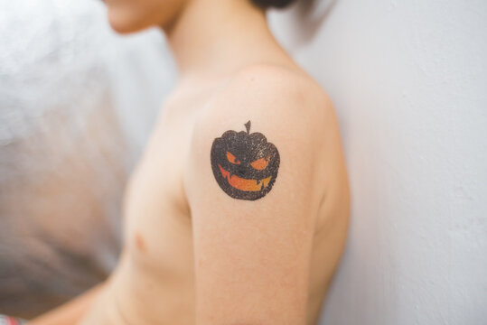 A child with a temporary tattoo on his shoulder depicting a sinister pumpkin.