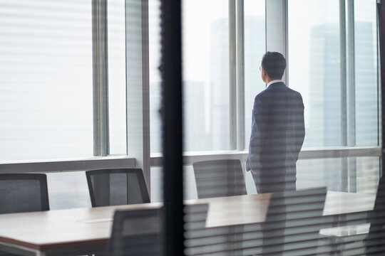 asian corporate executive standing in front of window thinking