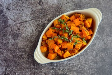 Baked pumpkin cubes with thyme on grey background. Top view