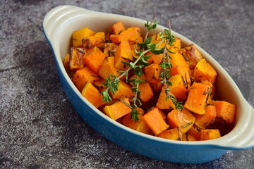Baked pumpkin cubes with thyme on grey background
