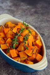 Baked pumpkin cubes with thyme on grey background