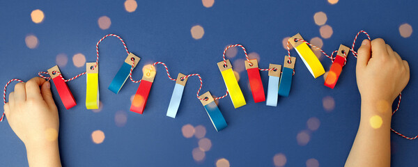 Handmade paper craft decorative garland with colorful lights in kid hands on classic blue...