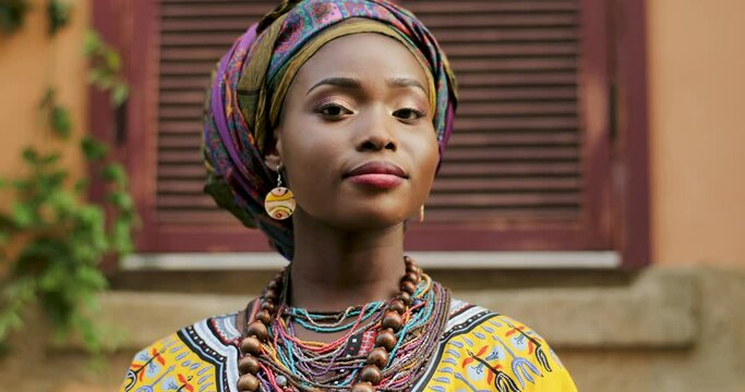 Close up of the face of the pretty young African woman in the traditional outfit looking at the side and smiling to the camera. Portrait. Outside.