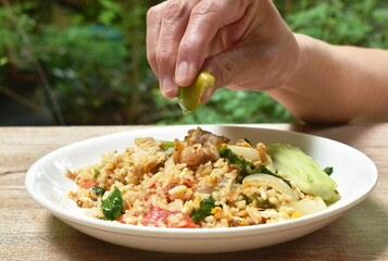 hand squeezing lemon to fried rice pork and Chinese kale with egg on plate 