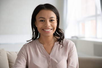 Profile picture of smiling African American young woman renter or tenant look at camera at home....