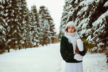 Beautiful portrait of young woman walking in green sweater, white dress, scarf and gloves in frosty winter park. Winter style and holidays.