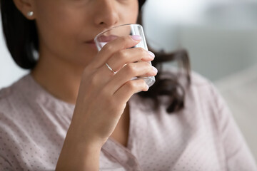 Crop close up of African American woman hold glass drink pure clean clear mineral water for body refreshment. Thirsty biracial female sip still liquid enjoy healthy lifestyle. Hydration concept.