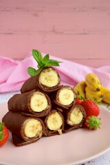 Delicious chocolate crepe rolls with banana and almond butter. Garnish with strawberries and mint leaves