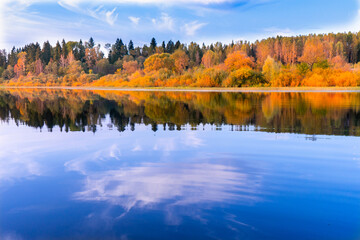 View of yellow autumn forest and blue lake water with reflection from a boat
