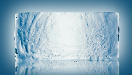 The rectangular block of pure transparent ice in cold blue tones on a mirroring surface with...