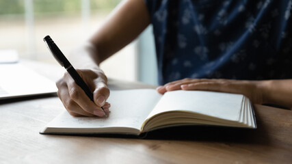 Crop close up of woman handwrite in notebook calculate expenses and expenditures at home. Female write make note in stationary notepad, manage family finances and budget or plan creating list.