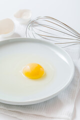 egg yolk on a plate  and whisk on white