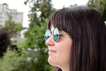 Close-up portrait of a young woman in round sunglasses, in light clothes on a clear, warm day in a city park. Weekend rest. Selective focus.