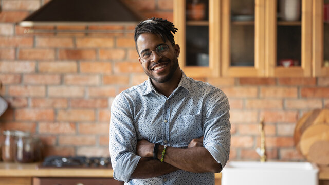 Portrait of smiling millennial African American man in glasses pose in modern renovated home kitchen. Happy young 20s biracial male tenant or renter in spectacles satisfied with good quality service.