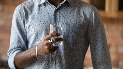 Crop close up of African American man hold glass recommend drinking clean pure mineral still water for body refreshment. Biracial guy follow healthy lifestyle. Wellness, hydration, diet concept.