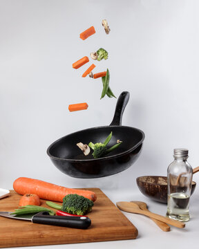 Chopped Sliced Diced Carrot Broccoli White Button Mushroom Red Chili Flying Dropping Gravity Defying On Floating Elevated Metal Frying Pan Cooking Board Bowl Oil Knife On White Background