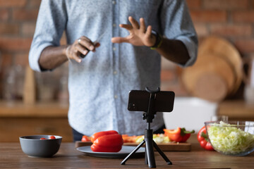 Crop close up of African American male chef vlogger shoot cooking food vlog blog on smartphone at home kitchen. Biracial man record recipe or tutorial on cellphone preparing healthy vegetarian dish.