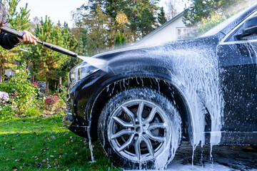 A man washes his car at home in the garden using a high-pressure washer with foam