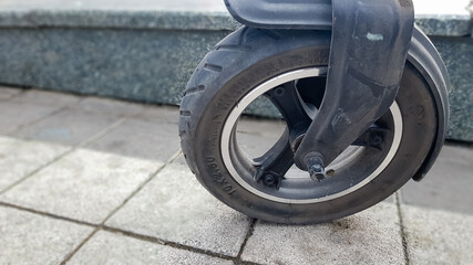 Scratched and damaged front wheel of an electric scooter on a city street against the background of paving slabs. Old e-scooter wheel. Modern technologies. Eco transport is provided for rent.