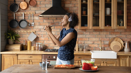 Overjoyed millennial African American woman have fun cooking healthy tasty breakfast in home...