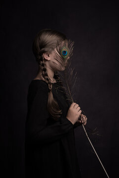 Classic studio portrait of a woman with a  peacock feather hiding her face in painterly Rembrandt style