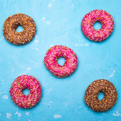 Glazed doughnuts with pink and chocolate icing with sprinkles on a blue background,space for text