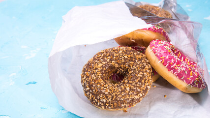 Glazed doughnuts with pink and chocolate icing with sprinkles in a package in a package on a blue background,space for text