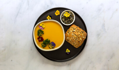 Autumn vegan pumpkin cream soup with edible flowers, seeds and bread