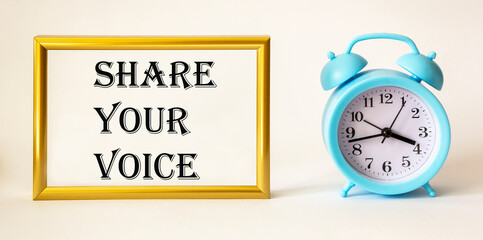 Share your voice written on gold photo frame next to alarm clock on white background.