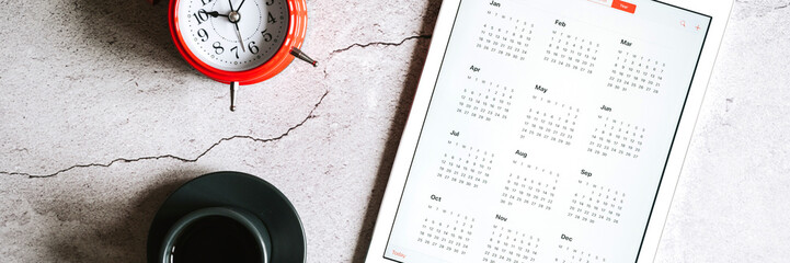 a tablet with an open calendar for 2021 year, a cup of coffee,  and a red alarm clock on a gray...